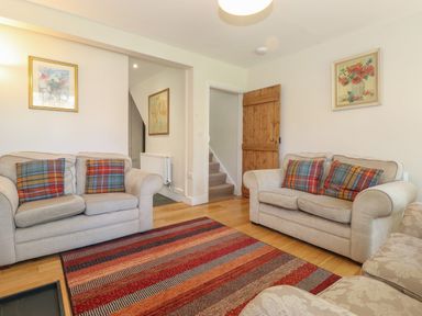 A living room with two beige sofas with plaid cushions a striped rug and wooden door at High Stile in Seatoller near Rosthwaite