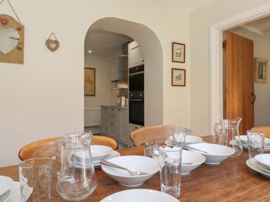 A dining table set with white bowls, plates, spoons, glasses, and glass pitchers in a room with an arched doorway leading to a kitchen at High Stile in Seatoller near Rosthwaite