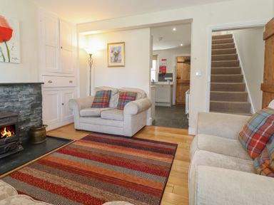 A living room with two beige sofas with plaid cushions a striped rug a fireplace and a view into a kitchen and stairs at High Stile in Seatoller near Rosthwaite