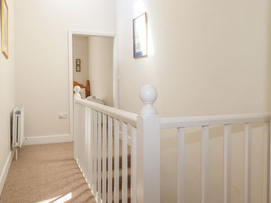 A hallway with beige carpet and white wooden railing with a bedroom visible at the end at High Stile Seatoller near Rosthwaite