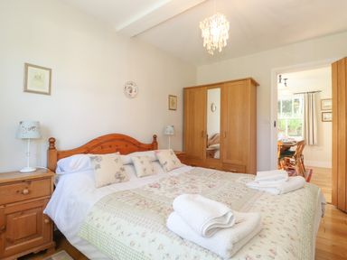 A bedroom with a double bed, wooden bedside tables with lamps, a wooden wardrobe with a mirror, and folded towels on the bed at High Stile in Seatoller near Rosthwaite