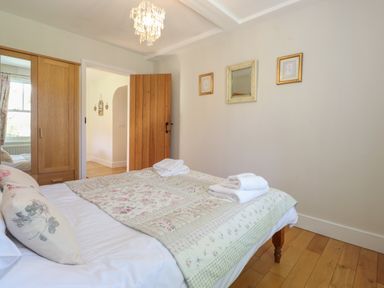 A bedroom with a bed covered in floral bedding and folded towels a wooden wardrobe and a wooden door with framed pictures and a mirror on the wall at High Stile in Seatoller near Rosthwaite