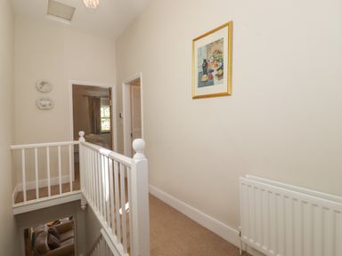 A hallway with a white railing beige carpet framed artwork and two decorative plates on the wall at High Stile in Seatoller near Rosthwaite