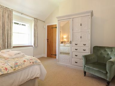 A bedroom with a bed covered with a quilt and towels a wardrobe with a mirrored door a green armchair a wooden door and a window with curtains at High Stile Seatoller near Rosthwaite