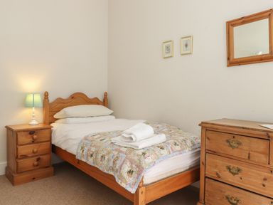 A bedroom with a wooden single bed with pillows and a quilt a bedside table with a lamp and a wooden chest of drawers with a mirror on the wall at High Stile in Seatoller near Rosthwaite
