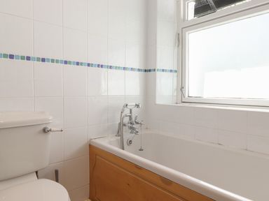 A bathroom with a toilet and a bathtub next to a frosted window at High Stile in Seatoller near Rosthwaite