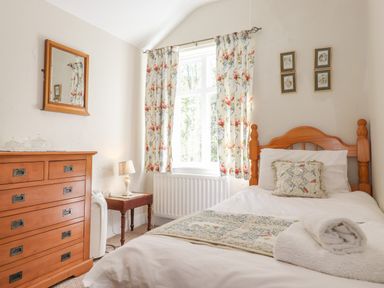 A bedroom with a single bed wooden dresser floral curtains and a small table with a lamp at High Stile in Seatoller near Rosthwaite