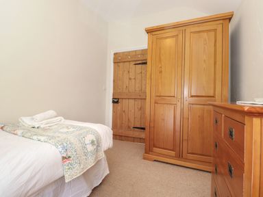 A bedroom with a bed covered in white linens a wooden wardrobe a wooden dresser and a wooden door at High Stile in Seatoller near Rosthwaite