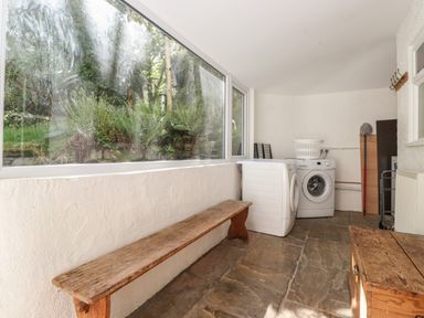 A laundry room with washing machines a wooden bench and large windows showing greenery outside at High Stile in Seatoller near Rosthwaite