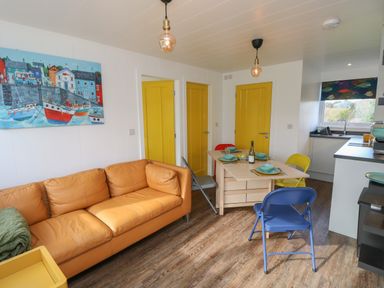 A living room with a tan sofa yellow doors a wooden dining table with colorful chairs and a kitchen area at Nanny's Little House in Sandown