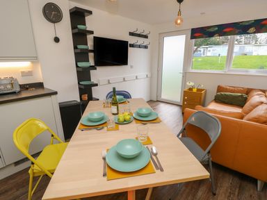 A dining area with a wooden table set with plates and bowls next to a kitchen counter and orange sofa at Nanny's Little House in Sandown