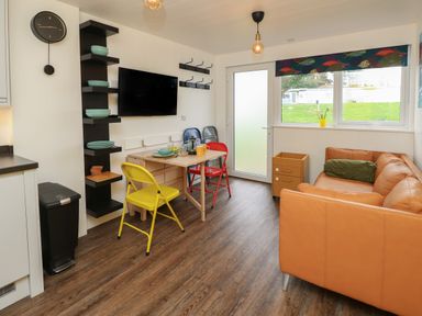 A small dining area with colorful chairs a wall-mounted television and a brown sofa near a window at Nanny's Little House in Sandown