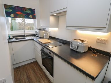 A kitchen with a sink, toaster, kettle, microwave oven, stovetop, oven, and wooden floor at Nanny's Little House in Sandown
