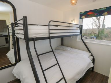 A bedroom with a metal bunk bed next to a window with a fish patterned blind and a large mirror on the wall at Nanny's Little House in Sandown