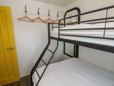 A bedroom with a black metal bunk bed a yellow door hangers on hooks and a large mirror at Nanny's Little House in Sandown