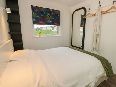 A bedroom with a bed white bedding window with fish patterned blind and a mirror with hooks on the wall at Nanny's Little House in Sandown