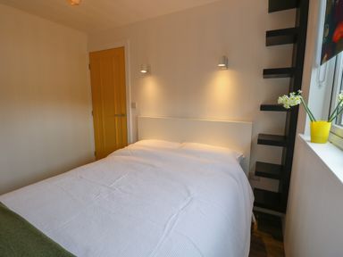 A bedroom with a white bedspread a yellow door and a window with flowers at Nanny's Little House in Sandown