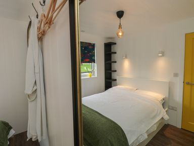 A bedroom with a bed white bedding green blanket window with floral curtain and yellow door at Nanny's Little House in Sandown
