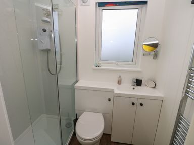 A bathroom with a shower cubicle a toilet a sink with cabinets a frosted window and a wall mounted mirror at Nanny's Little House in Sandown