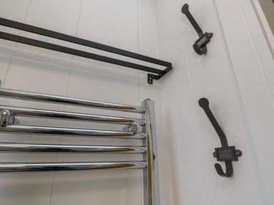 A wall with two black hooks a chrome towel rack and a black rectangular shelf bracket at Nanny's Little House in Sandown