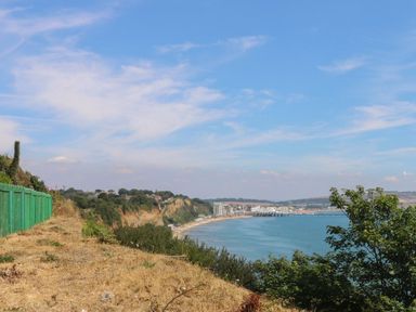 A coastal cliff with a green fence and view of a beach and buildings in the distance at Nanny's Little House in Sandown