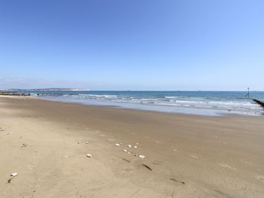 A sandy beach with scattered shells and footprints and calm sea waves under a clear sky at Nanny's Little House in Sandown