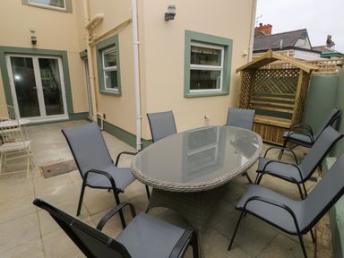 An outdoor patio with an oval glass table surrounded by six chairs and a wooden bench at Stones Throw in Tenby