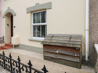 A house exterior with a window a door a wooden storage box and a metal fence at Stones Throw in Tenby