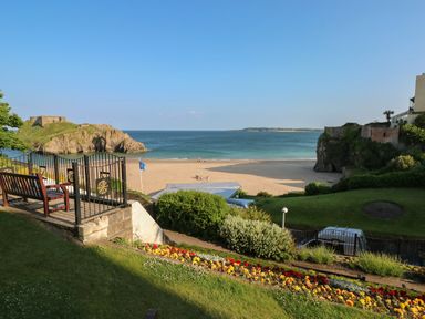 A garden with flower beds and benches overlooking a sandy beach and ocean at Stones Throw in Tenby