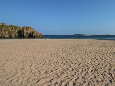 A sandy beach with a rocky cliff on the left and the sea in the background at Stones Throw in Tenby