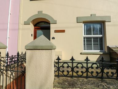 The exterior of a house with a red door window with shutters and black metal fence at Stones Throw in Tenby