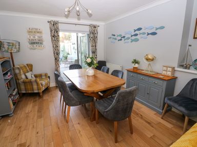 A dining room with a wooden table and gray chairs a yellow plaid armchair a gray sideboard and fish wall decorations at Stones Throw in Tenby