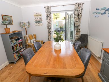 A dining room with a wooden table and chairs a bookshelf armchairs and a door opening to a patio at Stones Throw in Tenby