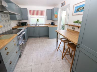 A kitchen with blue cabinets wooden countertops a tiled floor and two stools at Stones Throw in Tenby