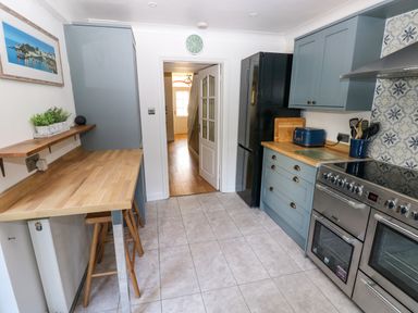 A kitchen with wooden countertops blue cabinets a black refrigerator a stove and a wooden breakfast bar at Stones Throw in Tenby