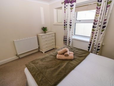 A bedroom with a bed folded towels a chest of drawers and a window with patterned curtains at Stones Throw in Tenby