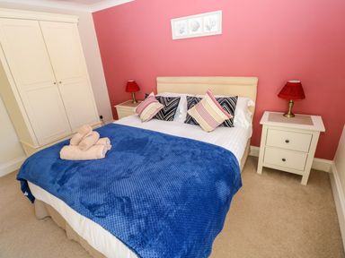A bedroom with a double bed blue blanket pillows towels bedside tables lamps and a wardrobe at Stones Throw in Tenby