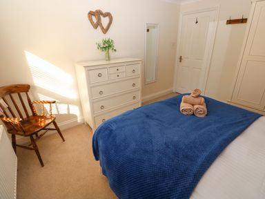 A bedroom with a wooden chair a chest of drawers a mirror and bed with blue cover and folded towels at Stones Throw in Tenby