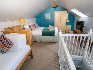 A bedroom with two beds a wooden wardrobe a TV and a skylight window at Stones Throw in Tenby