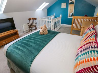 A bedroom with a bed a wooden chair a TV on a wooden stand and a desk at Stones Throw in Tenby