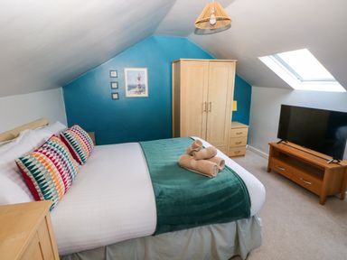 A bedroom with a double bed colorful pillows a wooden wardrobe bedside tables a television and a skylight window at Stones Throw in Tenby