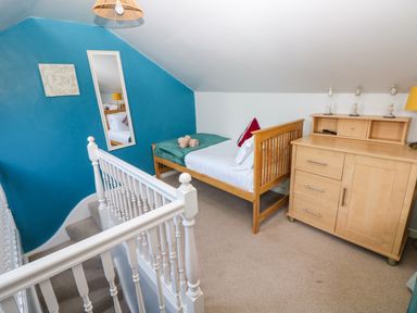 A bedroom with a wooden bed next to a wooden dresser and a blue accent wall at Stones Throw in Tenby