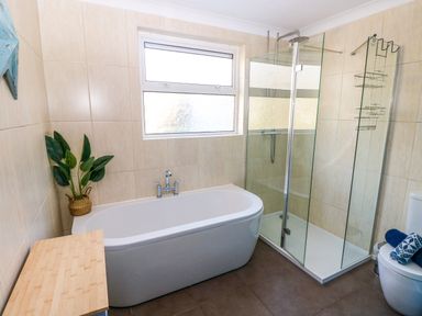 A bathroom with a bathtub a glass shower enclosure a toilet and a wooden cabinet at Stones Throw in Tenby