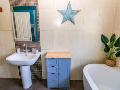 A bathroom with a white pedestal sink a blue cabinet a white bathtub a plant in a basket and a blue star wall decor at Stones Throw in Tenby