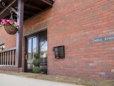 Front door area of a brick house with a black mailbox hanging on the wall a potted plant with three green spheres and a hanging basket with pink flowers at Mill End in Eamont Bridge near Penrith