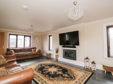 A living room with leather sofas a patterned rug a wall mounted tv and two chandeliers at Mill End in Eamont Bridge near Penrith