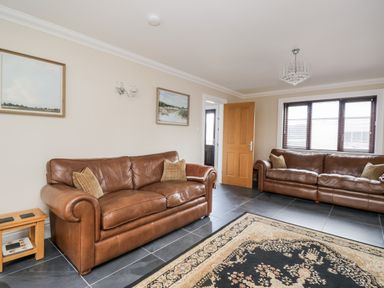 A living room with two brown leather sofas a wooden side table paintings on the wall and a patterned rug on a tiled floor at Mill End in Eamont Bridge near Penrith