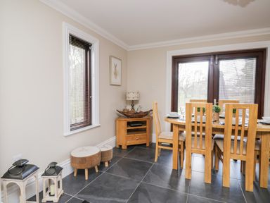 A dining area with wooden chairs and a table near glass doors and a window with stools and lanterns in the corner at Mill End in Eamont Bridge near Penrith