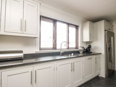 A kitchen with white cabinets a black countertop a sink under a window and stainless steel appliances at Mill End in Eamont Bridge near Penrith