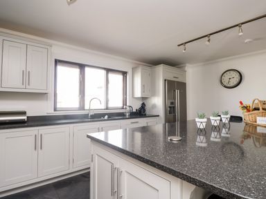 A kitchen with white cabinets a gray countertop a refrigerator a clock on the wall and small potted plants on a kitchen island at Mill End in Eamont Bridge near Penrith